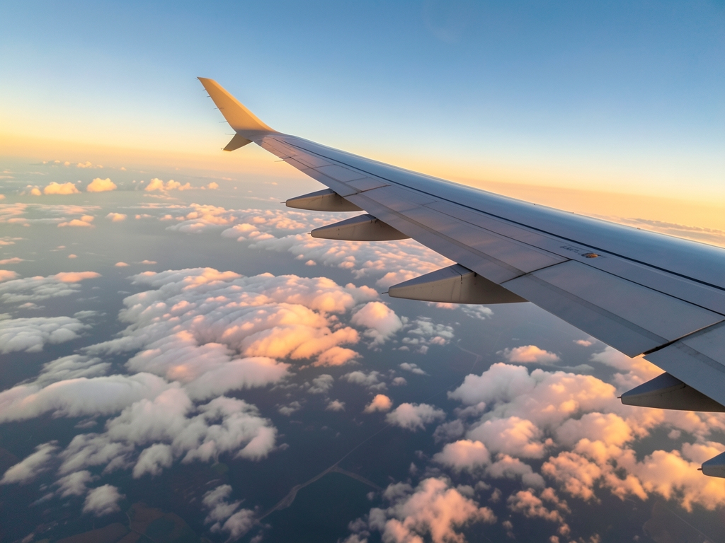 Aircraft wing above layered summer clouds sunrise with