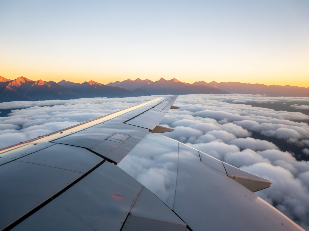 Airplane wing above soft clouds sunset with warm