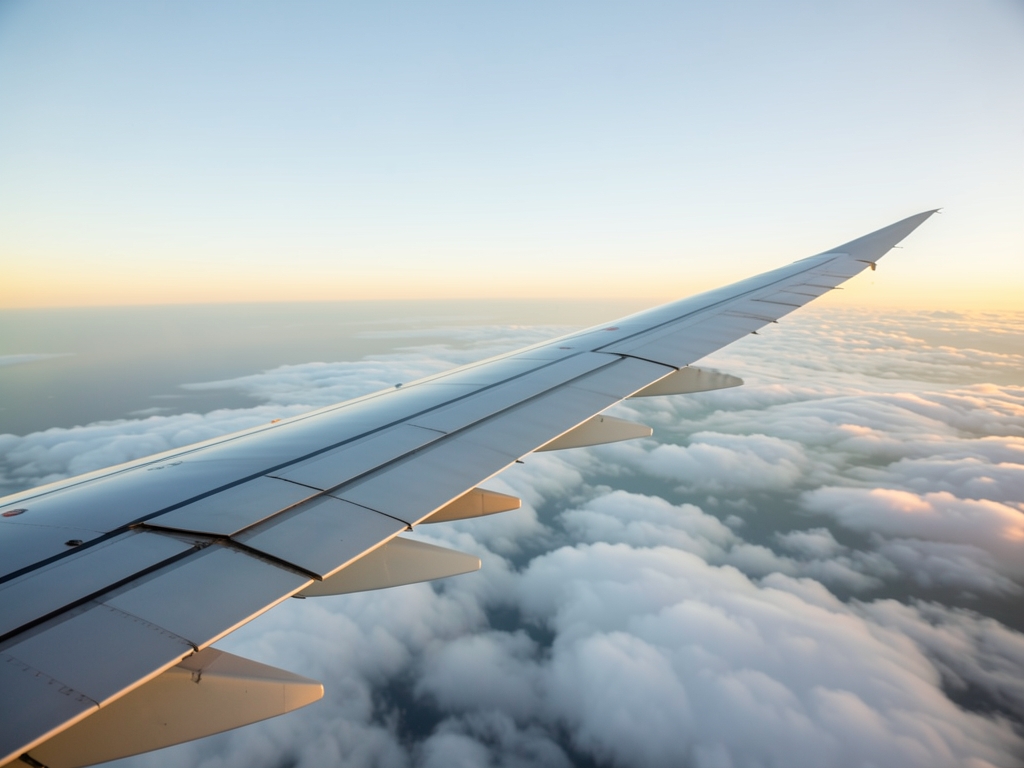 Airplane wing over vast ocean clouds sunrise with