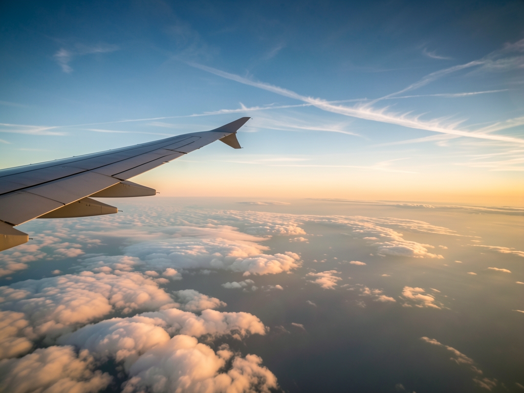 Airplane wing above clouds sunset silver aluminum warm