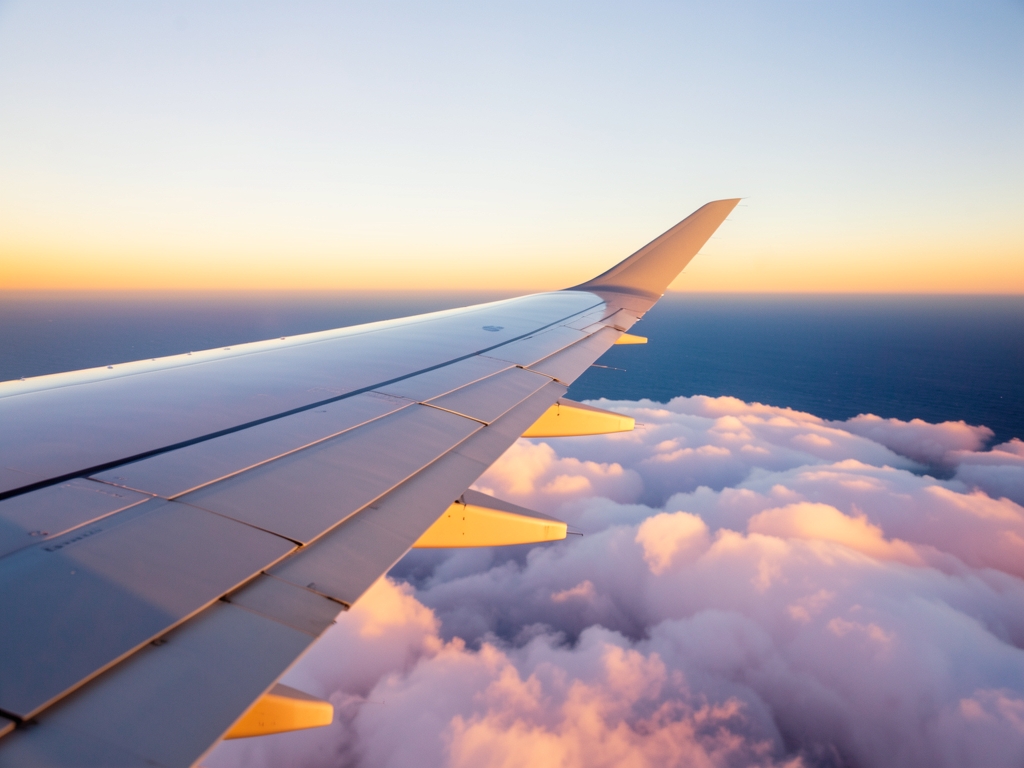 Airplane wing over vast ocean clouds golden sunset