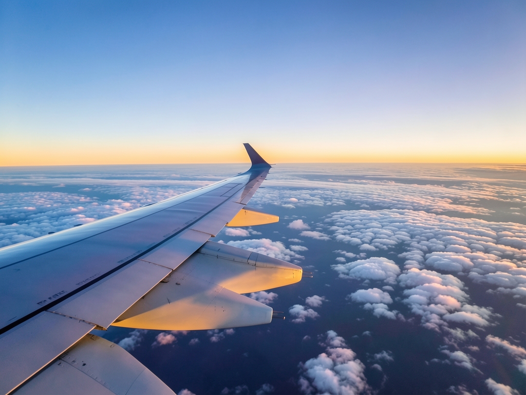Airplane wing over vast layered clouds golden sunset